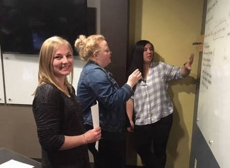 Three women in front of a whiteboard with code on it
