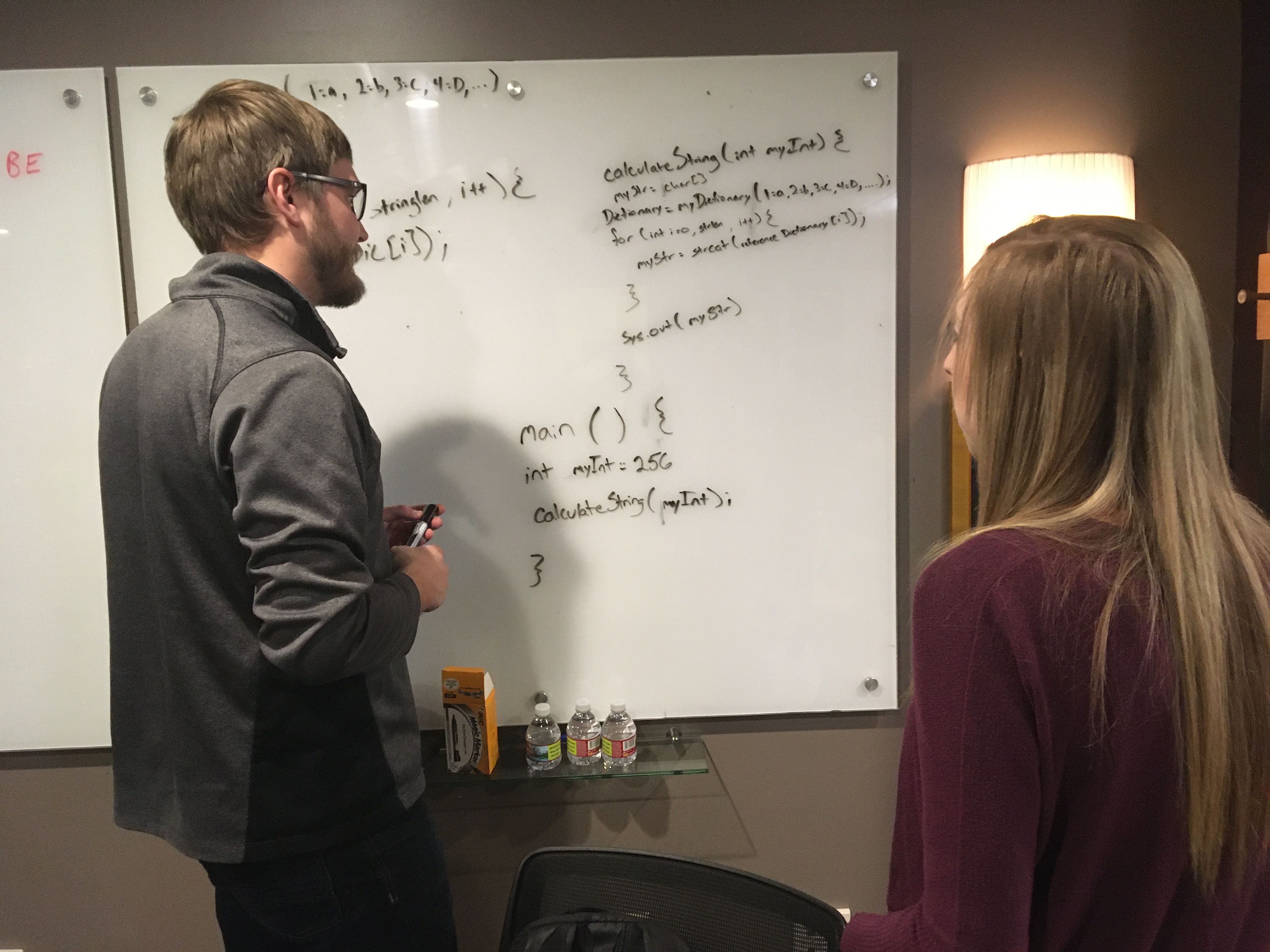 Man and a woman writing code on a whiteboard.